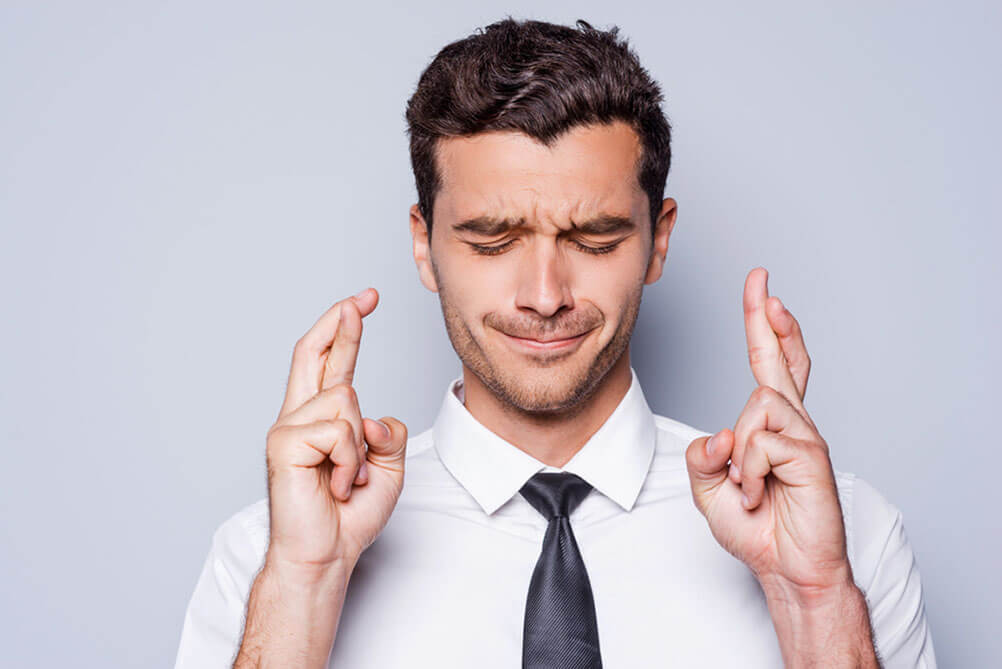 Man closing eyes and crossing fingers for luck